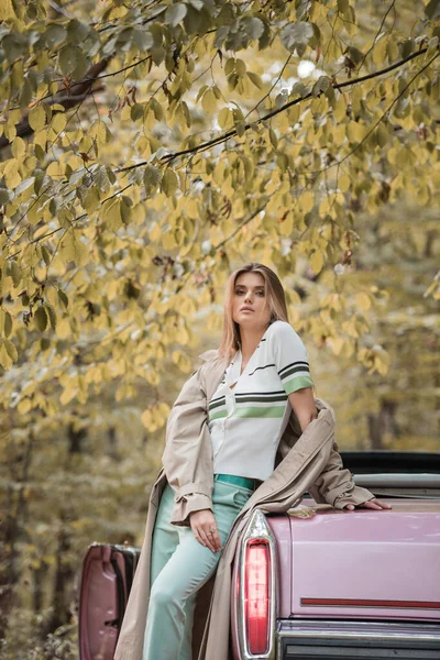 Young woman looking at camera while standing near vintage cabriolet in forest — Stock Photo