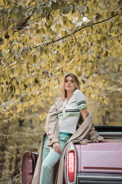 Jovem mulher olhando para a câmera enquanto está perto de cabriolet vintage na floresta — Fotografia de Stock