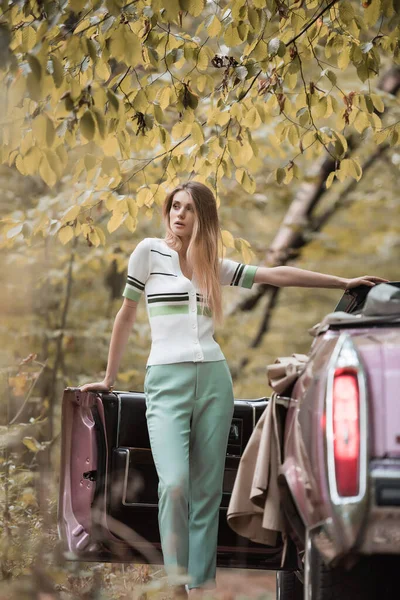 Young woman looking away while standing near open door of cabriolet on blurred foreground — Stock Photo
