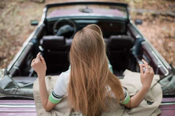 Back view of young woman sitting in vintage convertible car on blurred background — Stock Photo