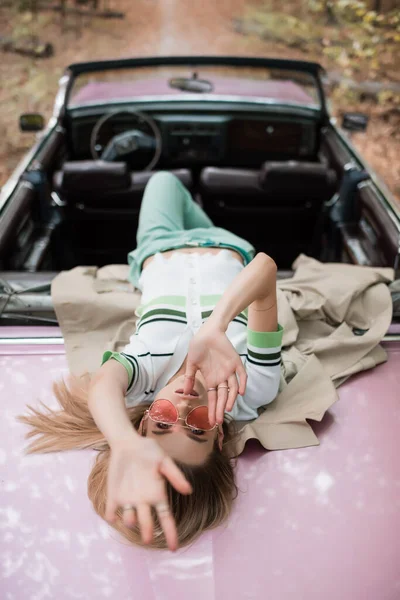 Overhead view of young woman looking at camera while lying on cabriolet on blurred background — Stock Photo