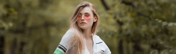 Молода стильна жінка в сонцезахисних окулярах дивиться в ліс, банер — стокове фото
