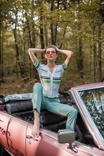 Stylish barefoot woman posing in vintage cabriolet with hands behind head — Stock Photo