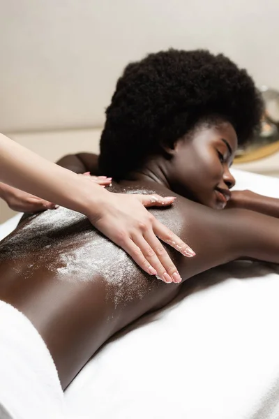Massaggiatore massaggio afro-americano donna con scrub nel salone spa — Foto stock