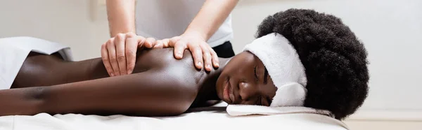Massagista massageando afro-americano mulher vestindo faixa branca no salão de spa, banner — Fotografia de Stock