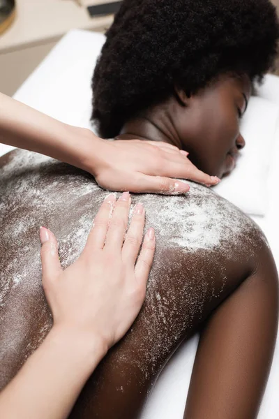 Vue rapprochée du masseur massant femme afro-américaine avec gommage dans le salon de spa — Photo de stock