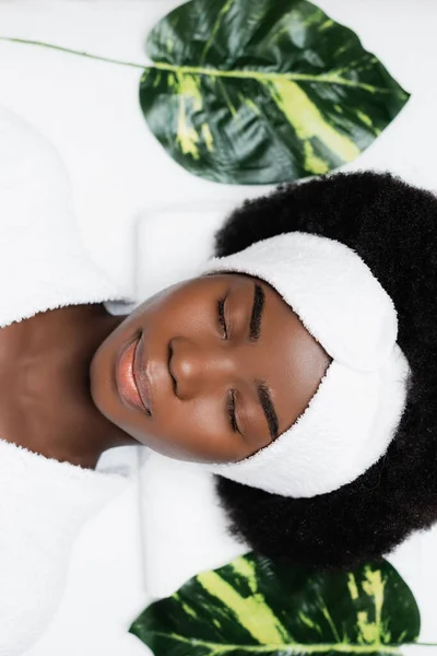 Vista superior da mulher americana africana com cabeça branca descansando perto de folhas verdes no salão de spa — Fotografia de Stock