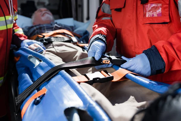 Focus selettivo della cintura di bloccaggio paramedica vicino al paziente sulla barella vicino all'auto dell'ambulanza — Foto stock