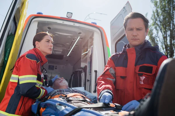 Concentration sélective des ceintures de verrouillage paramédicales sur civière avec patient âgé près d'un collègue et d'une ambulance — Photo de stock