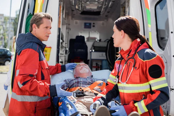 Selective focus of paramedic pointing at patient on stretcher near colleague in latex gloves and ambulance car — Stock Photo