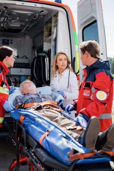 Selective focus of doctor looking at paramedic near patient on stretcher and ambulance car — Stock Photo