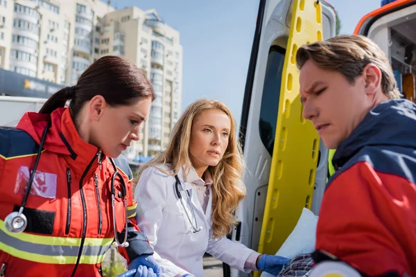 Selective focus of doctor looking at paramedic near ambulance car outdoor — Stock Photo