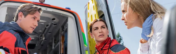 Website-Header des Arztes schaut sich Sanitäter in der Nähe von Rettungswagen im Freien an — Stockfoto