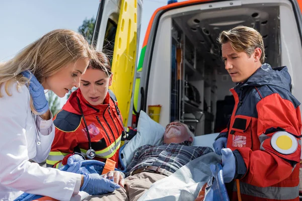 Foco seletivo do médico e paramédico olhando para o paciente na maca perto do carro da ambulância ao ar livre — Fotografia de Stock