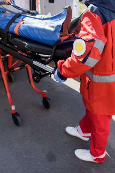 Cropped view of paramedic holding stretcher with patient near ambulance car outdoors — Stock Photo