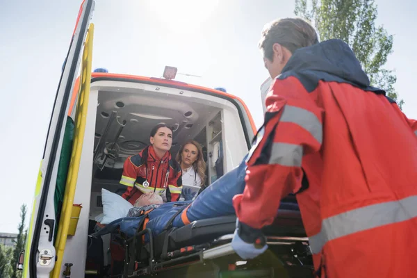 Selective focus of paramedics carrying stretcher with elderly man in ambulance car near doctor — Stock Photo