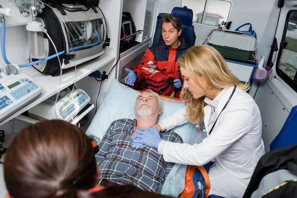 Селективный фокус врача в латексных перчатках, делающего кардиолегочную реанимацию пациенту рядом с парамедиками в машине скорой помощи — стоковое фото