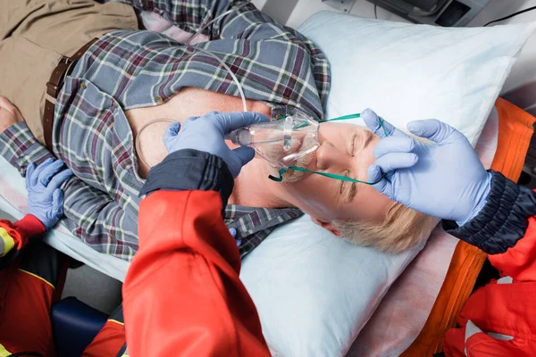 Foco seletivo de paramédico em luvas de látex usando máscara de oxigênio em paciente doente em carro de ambulância — Fotografia de Stock