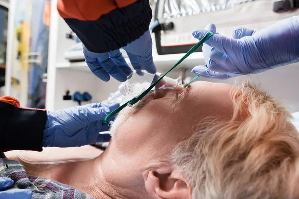 Selective focus of paramedics in latex gloves wearing oxygen mask on patient in ambulance auto — Stock Photo