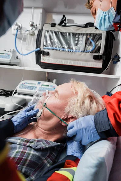 Selective focus of paramedics in medical masks and latex gloves wearing oxygen mask during first aid in ambulance car — Stock Photo