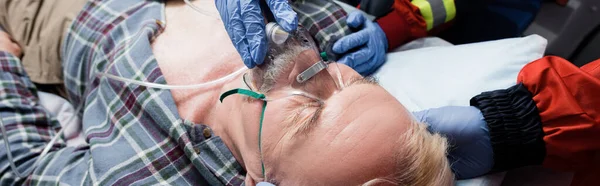 Panoramic shot of paramedic wearing oxygen mask on ill patient near colleague — Stock Photo