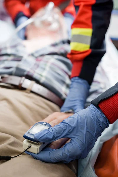 Selective focus of paramedic fastening heart rate monitor on ill patient in ambulance car — Stock Photo