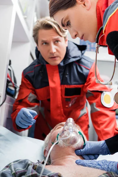 Selective focus of paramedic checking pulse of patient in oxygen mask near colleague in ambulance auto — Stock Photo