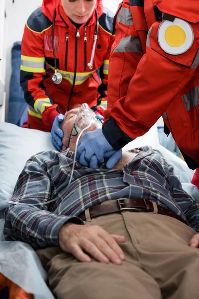 Foco seletivo dos paramédicos em luvas de látex fazendo ressuscitação cardiopulmonar ao paciente em máscara de oxigênio — Fotografia de Stock
