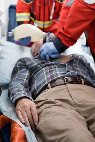 Selective focus of senior man lying in ambulance car near paramedics doing cardiopulmonary resuscitation — Stock Photo