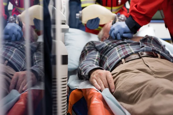 Selective focus of elderly patient lying in ambulance car while paramedics doing cardiopulmonary resuscitation — Stock Photo