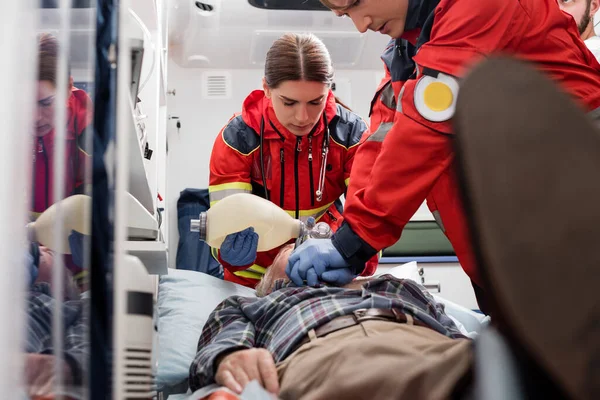 Selective focus of paramedics in uniform doing cardiopulmonary resuscitation to man during first aid — Stock Photo