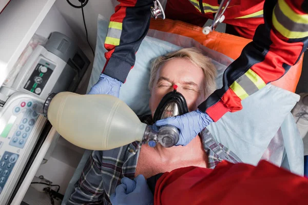 Vue du dessus des ambulanciers paramédicaux dans des gants de latex faisant de la réanimation cardiopulmonaire à un homme âgé — Photo de stock