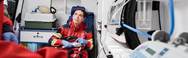 Foto panoramica del paramedico con kit di pronto soccorso seduto vicino al collega in ambulanza — Foto stock