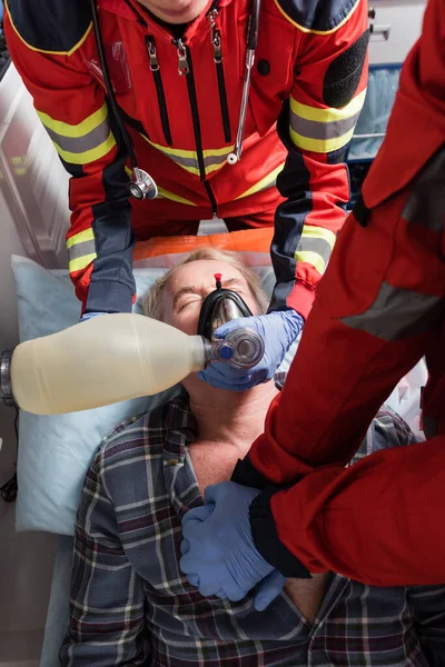Top view of paramedics in latex gloves doing cardiopulmonary resuscitation to senior man in ambulance auto — Stock Photo