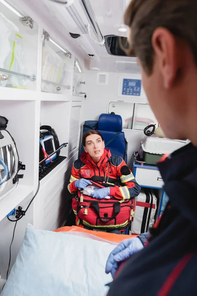 Enfoque selectivo de paramédico con botiquín de primeros auxilios mirando a colega en coche ambulancia - foto de stock