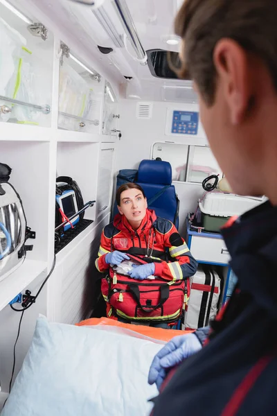 Selective focus of paramedic with first aid kit looking at colleague in ambulance car — Stock Photo