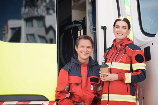 Paramedici con caffè per andare a guardare la macchina fotografica vicino ambulanza auto all'aperto — Foto stock