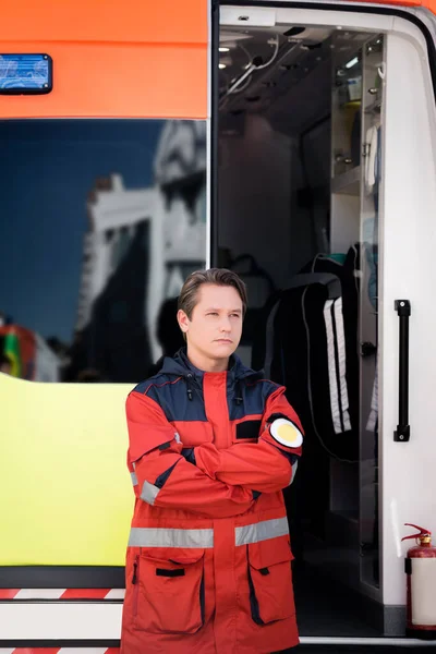 Paramédico con brazos cruzados de pie cerca de ambulancia auto al aire libre - foto de stock