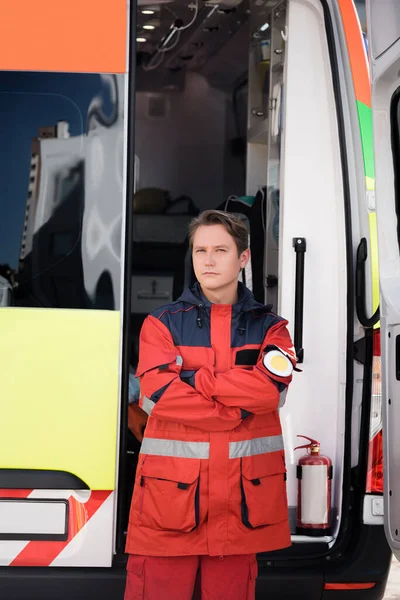 Sanitäter mit verschränkten Armen blickt in Kamera in der Nähe von Rettungswagen im Freien — Stockfoto