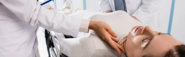 La inyección panorámica del médico que comprueba el pulso de la mujer en la camilla en la clínica - foto de stock