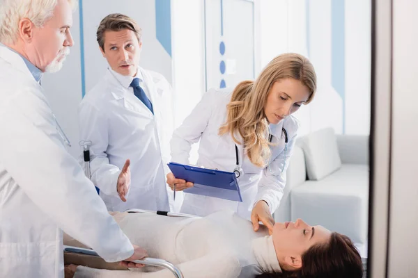 Concentration sélective du médecin pointant avec la main près de collègues avec presse-papiers et patient malade sur civière — Photo de stock