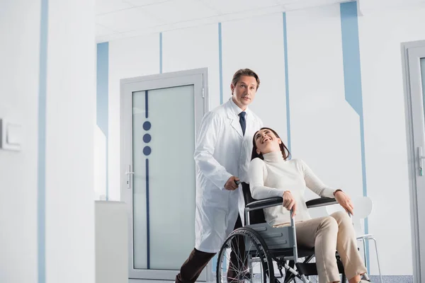 Enfoque selectivo del paciente excitado en silla de ruedas mirando al médico en la clínica - foto de stock