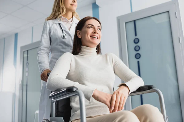 Selektiver Fokus der im Rollstuhl sitzenden Frau in der Nähe des Arztes im Flur der Klinik — Stockfoto