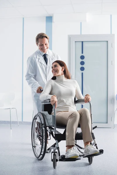 Selective focus of brunette woman sitting in wheelchair near doctor in white coat in hospital — Stock Photo