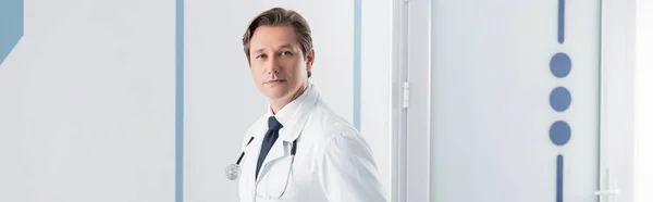 Panoramic shot of doctor in white coat looking at camera in hospital — Stock Photo