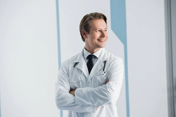 Доктор у білому пальто з схрещеними руками дивиться в лікарню — стокове фото