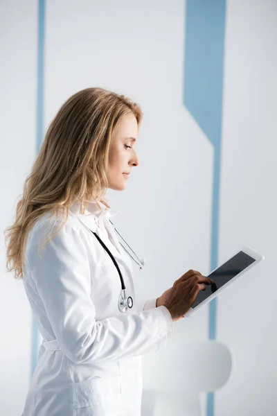 Vista laterale del medico biondo utilizzando tablet digitale in clinica — Foto stock
