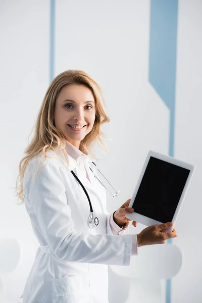 Medico biondo che mostra tablet digitale con schermo vuoto in clinica — Foto stock
