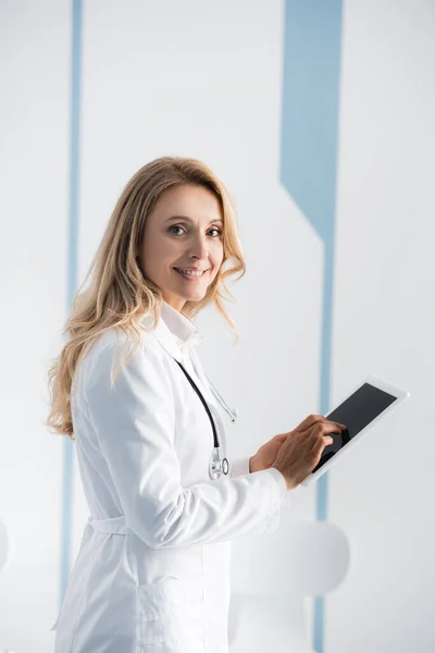 Vista lateral del médico mirando a la cámara mientras usa la tableta digital - foto de stock