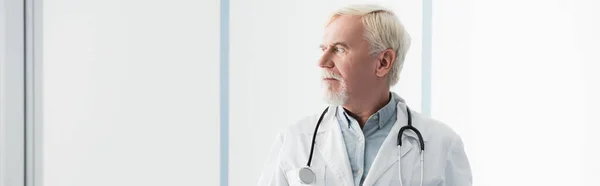Imagen horizontal del médico senior mirando hacia otro lado en la clínica - foto de stock